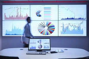 Businessman walking in front of graphs on screen showing forecasting of business.