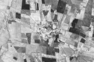 A black and white aerial photo of a large tell, surrounded by modern agricultural fields and small villages.