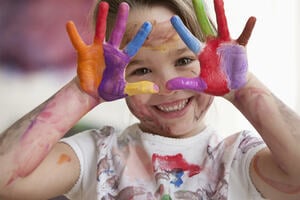 Messy Caucasian girl in art class with paints on here hands smiling.