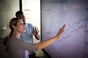 Two people looking at a chart on a large screen.