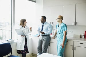 Female doctor leading medical team discussion in hospital exam room.